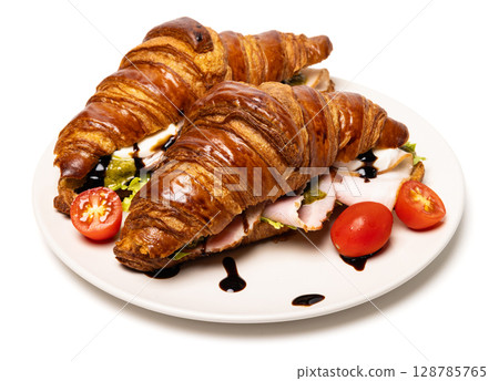 Two freshly baked classic delicious fresh organic croissants with ham, cheese, pesto sauce and tomatoes on a white ceramic plate isolated on white background Two freshly baked classic delicious fresh organic croissants with ham, cheese, pesto sauce and tomatoes on a white ceramic plate isolated on white background 128785765