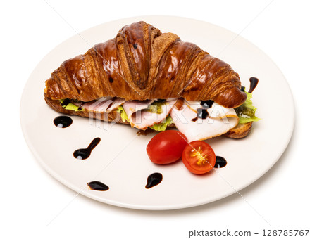 Freshly baked classic delicious fresh organic croissant with ham, cheese, pesto and tomatoes on white ceramic plate isolated on white background Freshly baked classic delicious fresh organic croissant with ham, cheese, pesto and tomatoes on white ceramic plate isolated on white background 128785767