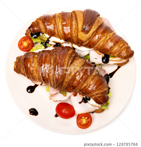 Two freshly baked classic delicious fresh organic croissants with ham, cheese, pesto sauce and tomatoes on a white ceramic plate isolated on white background Two freshly baked classic delicious fresh organic croissants with ham, cheese, pesto sauce and tomatoes on a white ceramic plate isolated on white background 128785768
