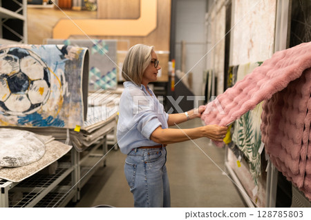 Woman shopping for home decor and carpets in a large retail store featuring various household items 128785803