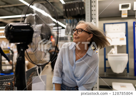 Woman shopping in a home improvement store enjoys a cooling breeze from a fan while exploring 128785804
