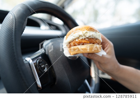 Asian lady holding hamburger to eat in car, dangerous and risk an accident. Asian lady holding hamburger to eat in car, dangerous and risk an accident. 128785911