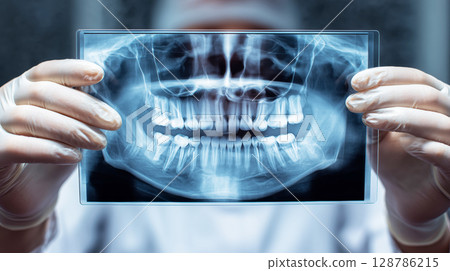 Close up view of a dental X ray image held by hands in medical gloves with blurred clinic background 128786215