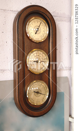 Classic barometer mounted on a wooden frame reflecting vintage craftsmanship in a cozy interior setting Classic barometer mounted on a wooden frame reflecting vintage craftsmanship in a cozy interior setting 128786329
