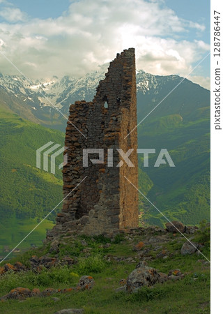Ancient architecture and ruins against mountain background . Remains of a destroyed tower . North Ossetia-Alania , Russia 128786447
