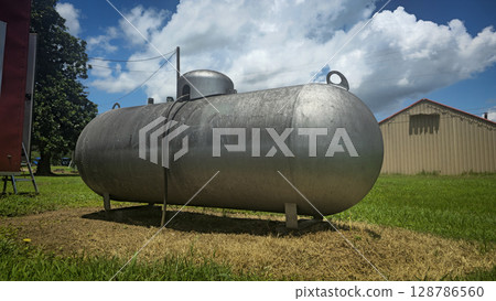 Large industrial propane tank installed outdoors on grass, designed for fuel storage and efficiency. The tank showcases durability and purpose for various industries and homes 128786560