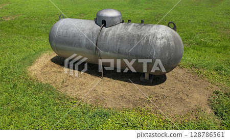 Large industrial propane tank installed outdoors on grass, designed for fuel storage and efficiency. The tank showcases durability and purpose for various industries and homes 128786561