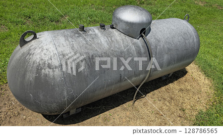 Large industrial propane tank installed outdoors on grass, designed for fuel storage and efficiency. The tank showcases durability and purpose for various industries and homes Large industrial propane tank installed outdoors on grass, designed for fuel storage and efficiency. The tank showcases durability and purpose for various industries and homes 128786565