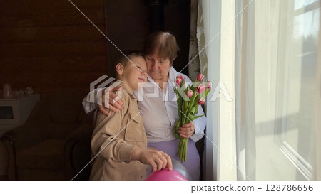 A cute boy gives his grandmother a bouquet of red tulips for her birthday, mother's day, anniversary. Warm family relationship between grandson and senior granny. 128786656