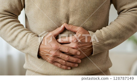 Man clutching stomach in pain. Abdominal discomfort and digestive health issue. Healthcare and medical concept for wellness. 128787149