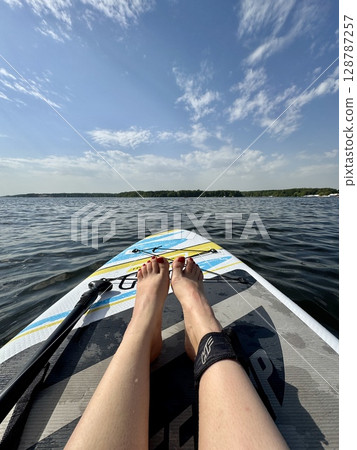 The legs of a girl riding a paddleboard in the summer. High quality photo The legs of a girl riding a paddleboard in the summer. High quality photo 128787257