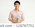 Smiling portrait of a young Japanese male nursery teacher holding a picture book White background 128787752