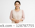 Smiling portrait of a Japanese female nursery teacher in her 40s with her hands folded in front of her, white background 128787755