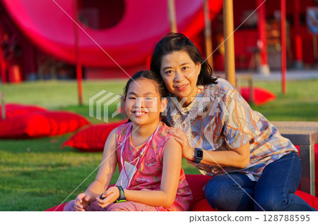 Portrait of an Asian middle-aged mother and daughter together in the garden at sunset, smiling faces, natural warm light. 128788595