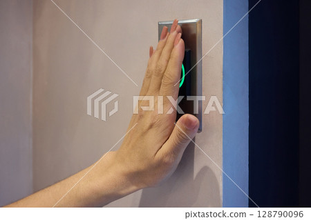 Hand Pressing a Modern Elevator Button That Features a Green Light Indicator for Operation 128790096