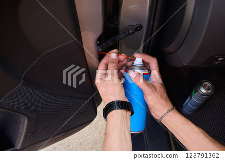 Applying spray lubricant to car door hinges helps keep them functioning smoothly Applying spray lubricant to car door hinges helps keep them functioning smoothly 128791362