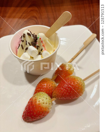 Vanilla soft serve with chocolate sprinkles and marshmallow, and strawberry on skewer, served on a white plate. 128791513