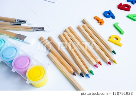 Colorful art supplies with brushes, pencils, and magnetic letters on white background Colorful art supplies with brushes, pencils, and magnetic letters on white background 128791928