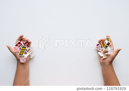 Child hands holding assorted toy traffic signs on white background Child hands holding assorted toy traffic signs on white background 128791929