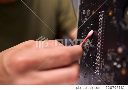 A Close Up View of a Hand Engaged in the Process of Cleaning a Circuit Board Component 128792181