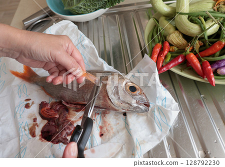 Anonymous gutting fresh fish on paper in kitchen. Food and organic seafood. 128792230