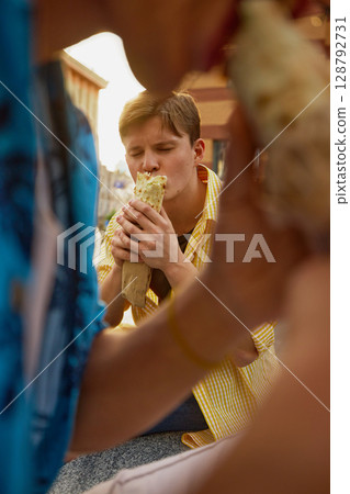 Young man closing eyes while taking a bite of shawarma with joy 128792731