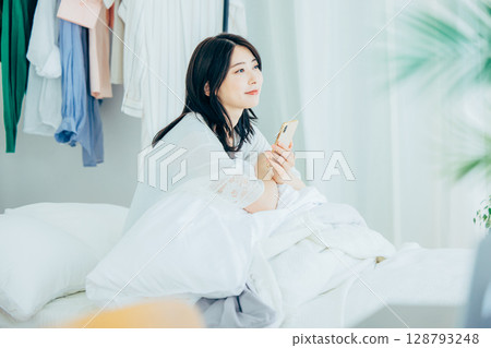 A young lady who manipulates a smartphone in bed A young lady who manipulates a smartphone in bed 128793248