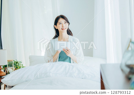 一位中年婦女在床上操作平板電腦 128793312