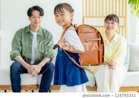 一個背著書包的女孩，她的父母在一旁看著 128793352