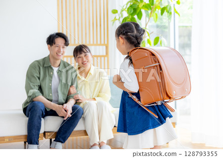 A girl carrying a school bag, her parents watching A girl carrying a school bag, her parents watching 128793355