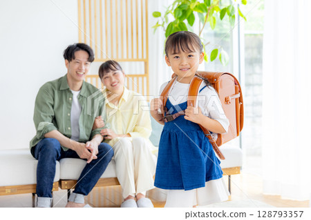 A girl carrying a school bag, her parents watching A girl carrying a school bag, her parents watching 128793357