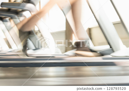 Mans legs running on treadmill in modern gym. Motion blur legs show speed and intensity. Workout session. Abstract sport background. Close up. Mans legs running on treadmill in modern gym. Motion blur legs show speed and intensity. Workout session. Abstract sport background. Close up. 128793520