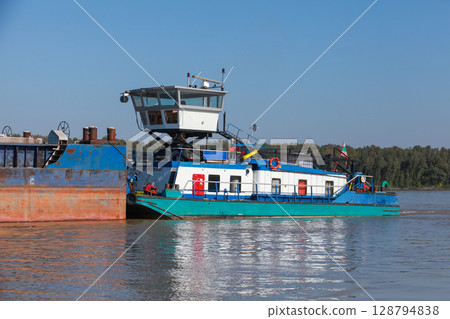 A blue and white tugboat moves a barge on Danube river, 128794838
