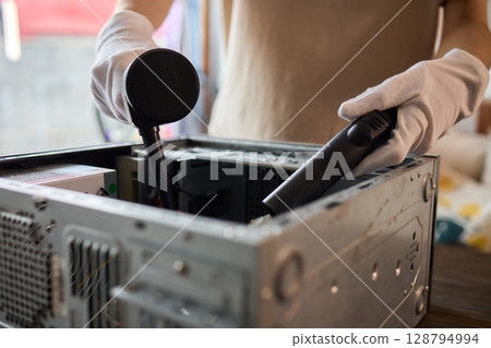 A man cleans a computer case with a vacuum in a bright room, stressing workspace tidiness A man cleans a computer case with a vacuum in a bright room, stressing workspace tidiness 128794994
