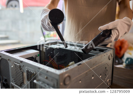 A man cleans a computer case with a vacuum in a bright room, stressing workspace tidiness A man cleans a computer case with a vacuum in a bright room, stressing workspace tidiness 128795009