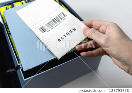 A woman's hand holds a return label over the blue box 128795828