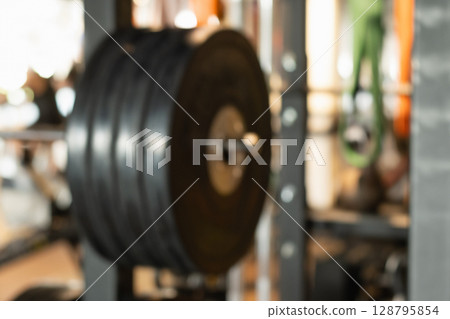 Abstract blurred gym background with sports fitness equipment barbell and weight plates in defocus. Sport background with space for design. 128795854