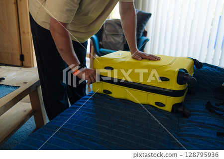 Man Packing Yellow Suitcase on Bed Before Travel 128795936