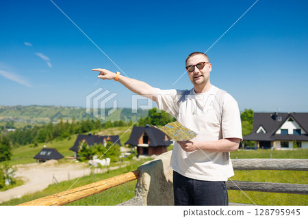 Smiling Man Pointing Ahead While Holding a Map in Mountain Village 128795945