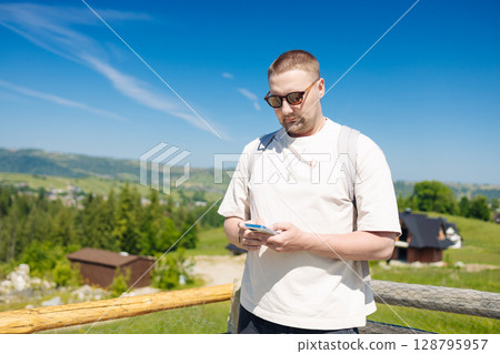 Man Using Smartphone Outdoors with Scenic Mountain View 128795957