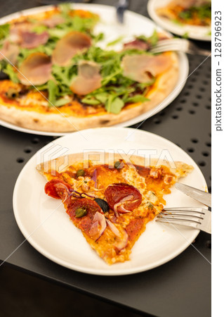Italian delicious pizza with prosciutto and salami pepperoni on a table in a restaurant or cafe Italian delicious pizza with prosciutto and salami pepperoni on a table in a restaurant or cafe 128796923