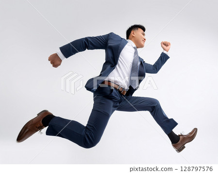 A businessman in a suit running and jumping 128797576