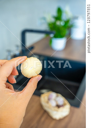 Female hand holding peeled Chinese single clove garlic. Fresh ingredient, natural flavor, and kitchen preparation. 128797851