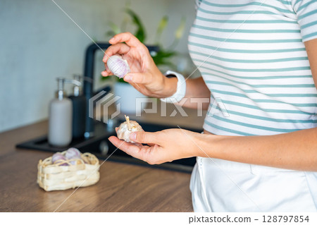 Hands of young woman holding Chinese single clove garlic and regular multi clove garlic, choosing ingredient for cooking. Culinary selection, natural food, and kitchen preparation. Hands of young woman holding Chinese single clove garlic and regular multi clove garlic, choosing ingredient for cooking. Culinary selection, natural food, and kitchen preparation. 128797854