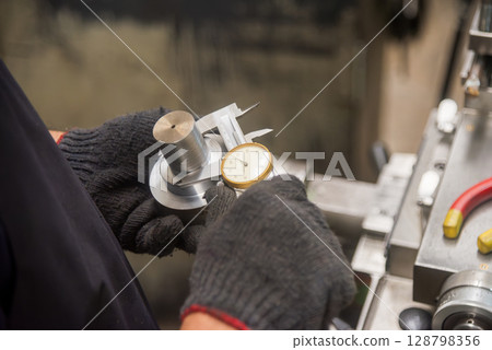 Close up scene the machine operator measuring dimension of metal shaft parts by dial Vernier caliper. 128798356
