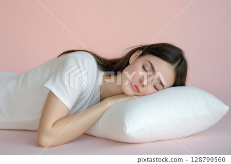 Calm young woman resting on her side on a smooth floor, with a pillow under her arm, minimalist and soft light background 128799560