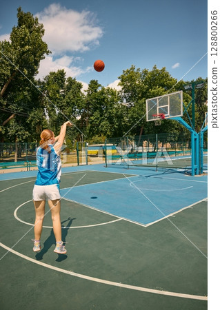Woman playing basketball on sunny outdoor court 128800266