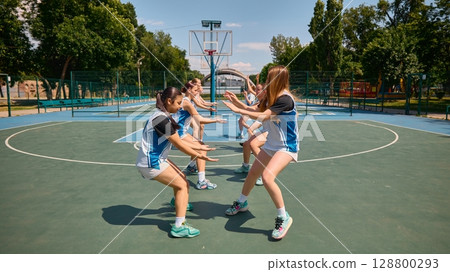Female basketball athletes engaging in defensive exercises on an outdoor court 128800293