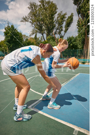 Two female basketball players engage in dribbling and shooting exercises on an outdoor court 128800324