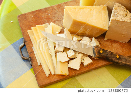 Close-up of sliced and crumbled hard cheeses with kitchen knife on rustic wooden board 128800773